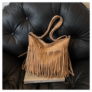 Brown faux suede tassel shoulder bag with retro fringe and gold metal buckle on a chair