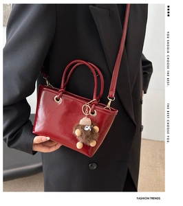 Detail of red glossy bucket bag with plush monster charm and golden hardware accents