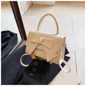 Detailansicht der cremefarbenen Lacklederhandtasche mit einer stylischen Dekoschleife