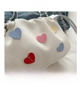 Detail of white striped fabric bag with colorful leather heart patches and silver chain