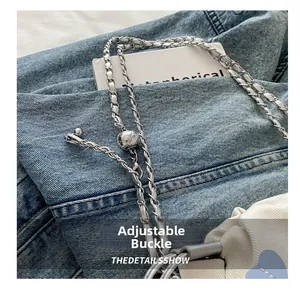Detail view of the adjustable metal ball buckle on a leather woven crossbody chain strap