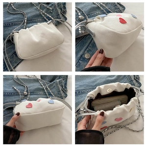 Detail view of white canvas crossbody bag with colorful heart patches and silver chain