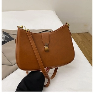 Close-up of brown leather shoulder bag with gold metal buckle on a beige blazer