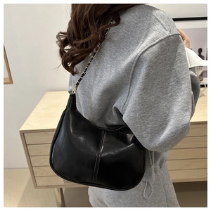 Détail du sac demi-lune en cuir noir avec coutures verticales et chaîne dorée