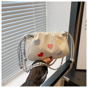 Detail of white drawstring bucket bag with colorful heart patches and silver chain strap