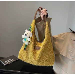 Detail of yellow plush tote bag with leather handle and cute bear charm decoration
