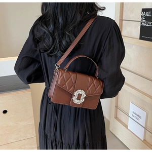 Brown quilted crossbody bag with rhinestone buckle worn by a model in a cozy library