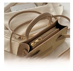 Detail view of a woven cream beige handbag showing the smooth golden zipper and texture