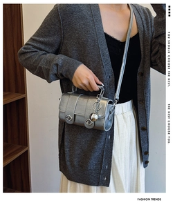 Detail van zilveren cilindrische crossbodytas met dubbele gesp en metalen kettinghanger