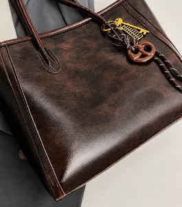 Detail of dark brown leather tote bag with vintage charms and visible stitching