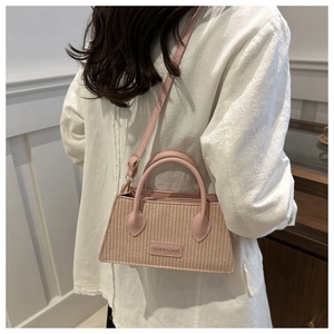 Close-up of pink woven handbag with leather handle and fashion brand logo detail