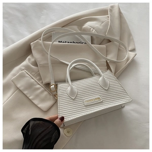 Close-up of white woven trapezoid bag featuring gold lettering and fine PU leather texture