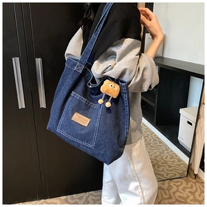 Detail view of large blue denim tote bag with leather logo patch and brown plush charm