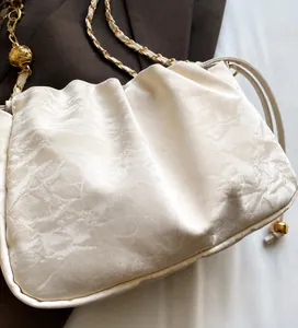 Détail du sac nuage plissé blanc montrant la texture soie et la chaîne à boule dorée