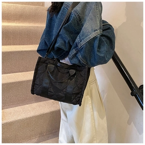 Detail of a black quilted crossbody bag with nylon fabric and adjustable strap worn by a model