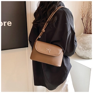 Detailed back view of a brown leather shoulder bag with a gold bow buckle on a model
