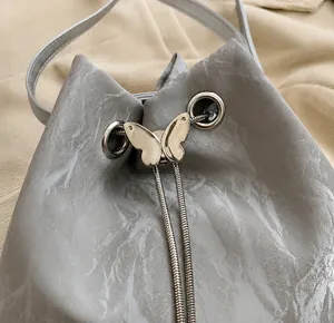 Detailansicht der grauen Marmor-Eimertasche mit goldenem Schmetterlingsverschluss