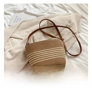 Detail showing the brown striped straw bucket bag with a slim leather shoulder strap