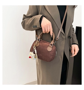 Brown suede crossbody bag with wooden handle and plush charm shown on trench coat