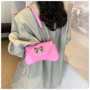 Detail of pink glossy shoulder bag with silver metal butterfly and chain strap on model