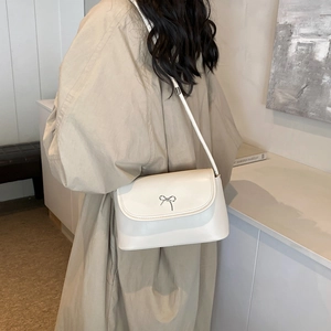 Sac bandoulière blanc crème avec boucle noeud argenté porté sur l'épaule, style minimaliste
