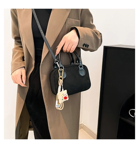 Detail of black suede Boston bag with double handles and plush animal pendant charm