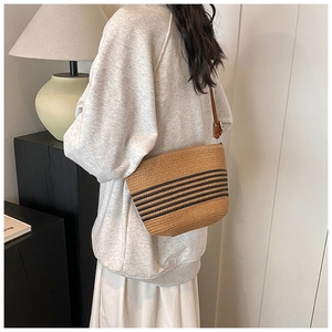 Detail of hand-woven straw bucket bag with black stripes and leather shoulder strap