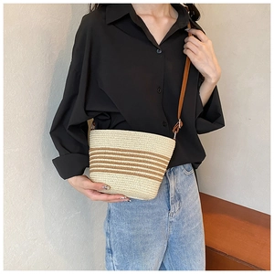 Detail of striped straw crossbody bag with brown leather strap worn by a model