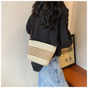 Detail of a beige woven straw bag with dark brown stripes and a leather shoulder strap