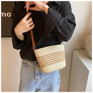 Detail of handwoven straw crossbody bag with brown stripes and thin leather strap