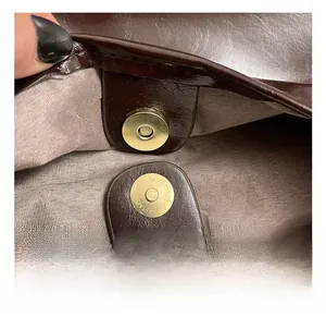 Detail of golden magnetic snap closures and premium oil-wax leather on dark brown tote bag