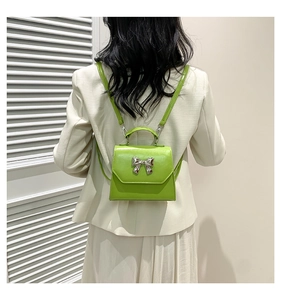 Detail shot of a green leather mini square bag with a silver bow buckle on the flap