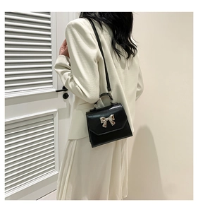 Detailed back view of a black crossbody bag with silver bow ornament on white outfit