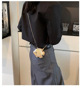 Detalle de un mini bolso metálico dorado con forma de pez y una fina correa de cadena