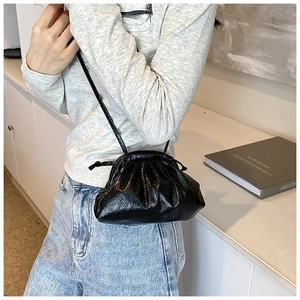 Model wearing a black glossy pleated dumpling bag with thin shoulder strap in minimalist room