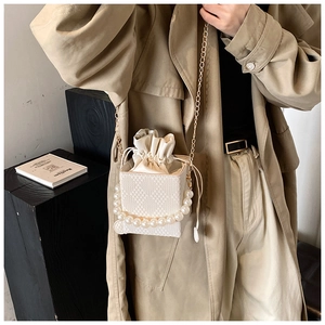 Detailansicht einer weißen Box-Tasche mit Perlengriff und Metallkette auf einem Trenchcoat