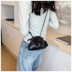 Detail of black pleated shell bag with sleek strap shown on a model in minimalist setting