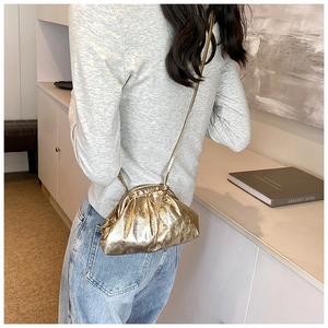 Sac pochette doré plissé avec fine bandoulière présenté sur un canapé élégant