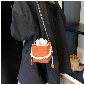 Detail der orangen Perlenhandtasche mit Webstruktur und Goldkette auf schwarzem Mantel