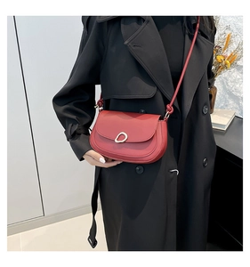 Sac à main croissant rouge chic avec boucle dorée porté sur un mannequin en trench-coat