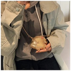 Detalle del bolso metálico dorado con forma de pez y textura de escamas con cadena
