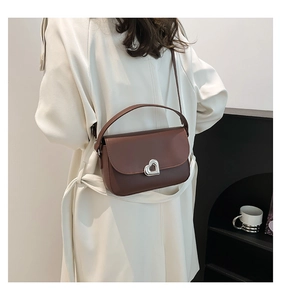 Detail view of caramel leather saddle bag with silver heart-shaped metal twist lock buckle