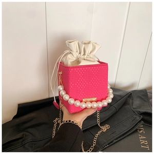 Detail der rosa geflochtenen Tasche mit Perlenkapitel und goldener Kette auf schwarzem Leder