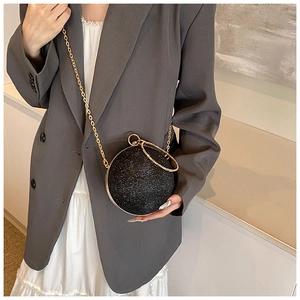 Close-up of a black glittery round evening bag with gold ring handle and chain strap detail