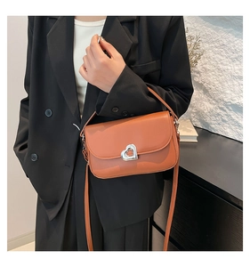 Detail of orange brown square bag featuring silver heart metal buckle on leather flap