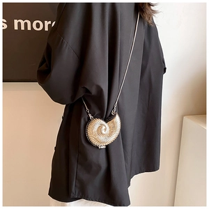 Golden nautilus-shaped metal mini bag with chain strap styled on a black shirt background