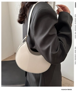 Side view of an off-white crescent shoulder bag worn over a charcoal grey suit