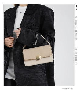 Detalle de bolso beige en contraste con gran hebilla dorada sobre americana negra