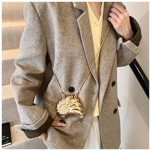 Detalle de un mini bolso bandolera dorado con forma de caracola y cadena de serpiente fina