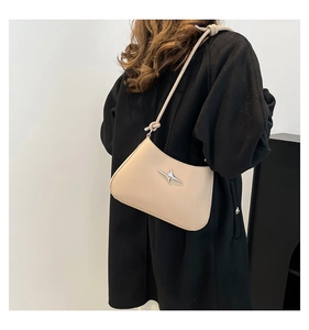 Bolso beige de media luna con hebilla de estrella plateada sobre un abrigo negro